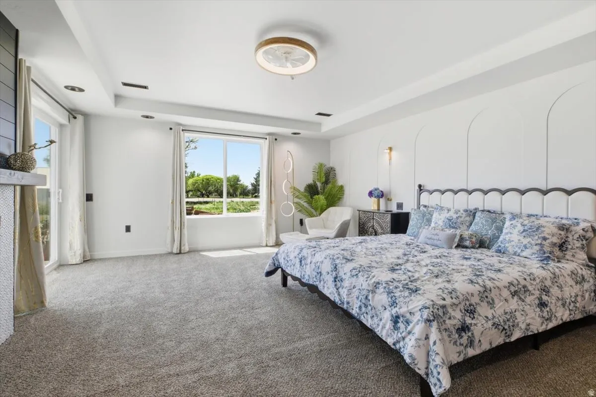 Carpeted room featuring a double tray ceiling with recessed lighting, large windows, and a built-in fireplace with a stone mantel