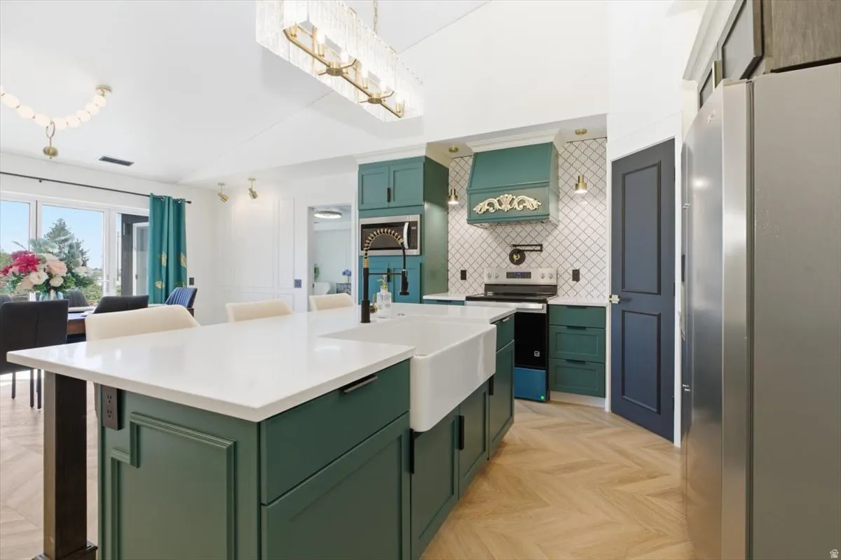Kitchen featuring an expansive island with a farmhouse sink and white countertop, herringbone wood-finish flooring, custom green cabinetry, a decorative range hood, and a geometric tiled backsplash