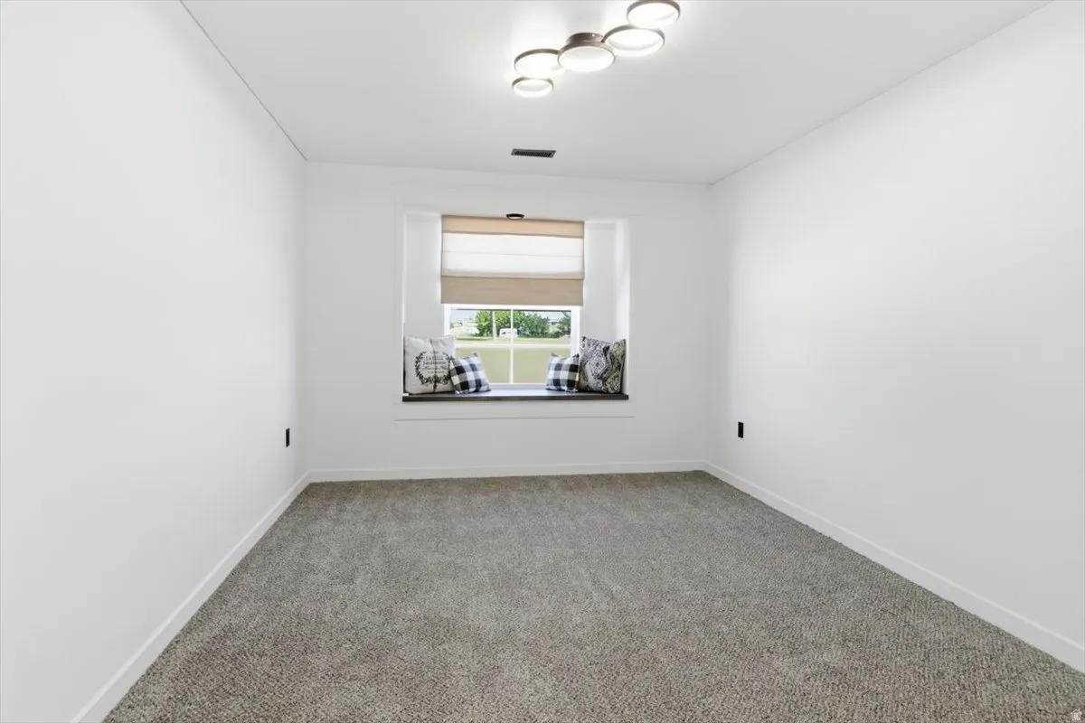 Recessed window seat with a custom cushion, neutral tone carpet, white baseboards, modern ceiling light fixture, and white wall finishes