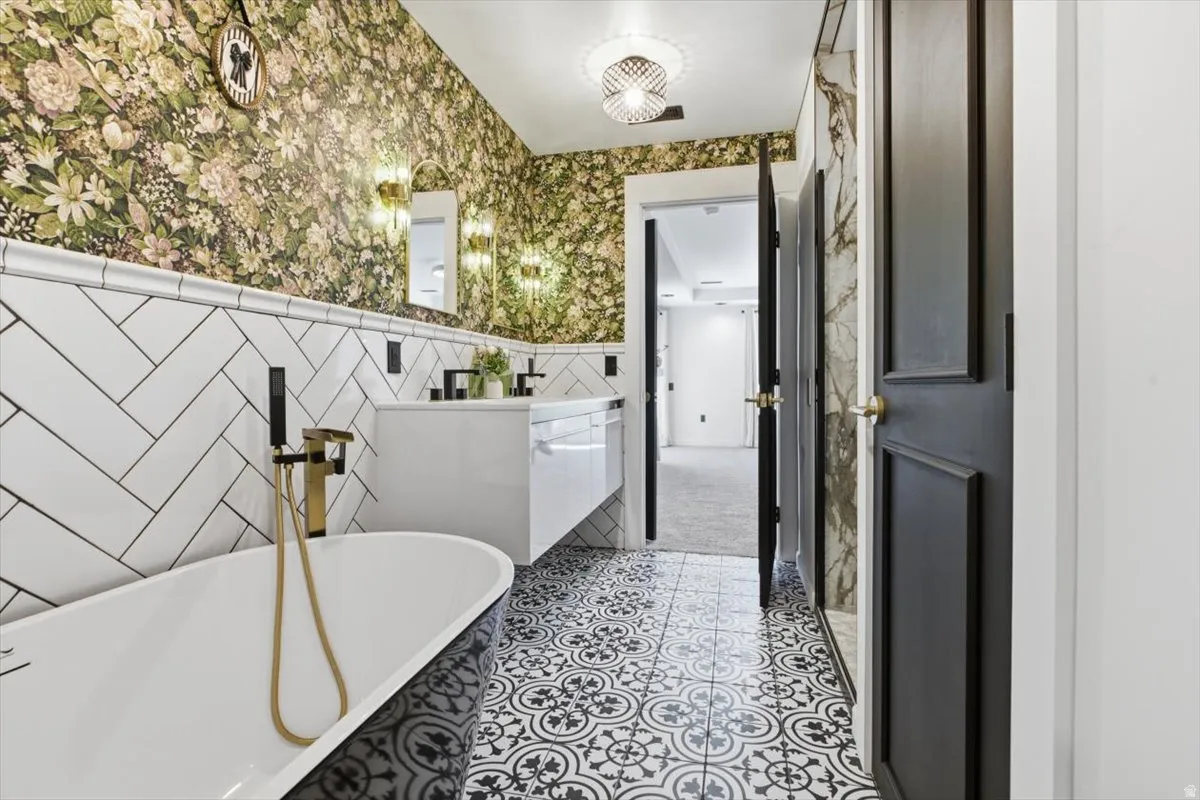 Bathroom featuring a clawfoot tub with a gold and black faucet, a floating double vanity with matte black fixtures, white subway tile in a herringbone pattern, and patterned floor tiling