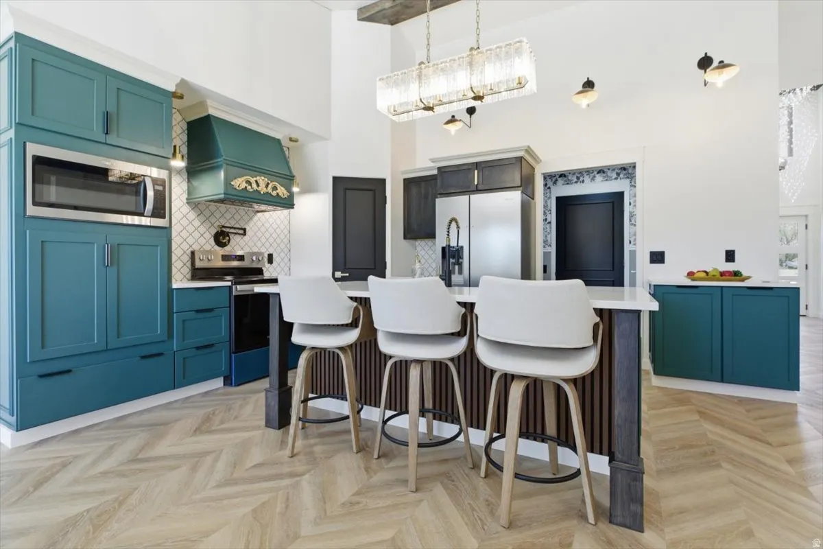 Chef's kitchen featuring teal cabinetry, stainless steel appliances, a decorative range hood, wood-finish herringbone flooring, and a central island with countertop seating
