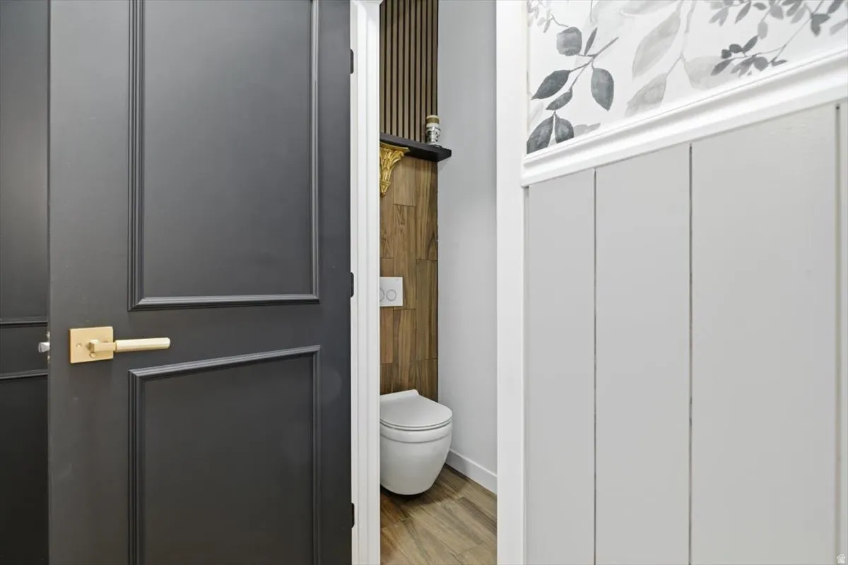 Powder room featuring a wall-mounted toilet, wood-finish flooring, and a decorative wall panel