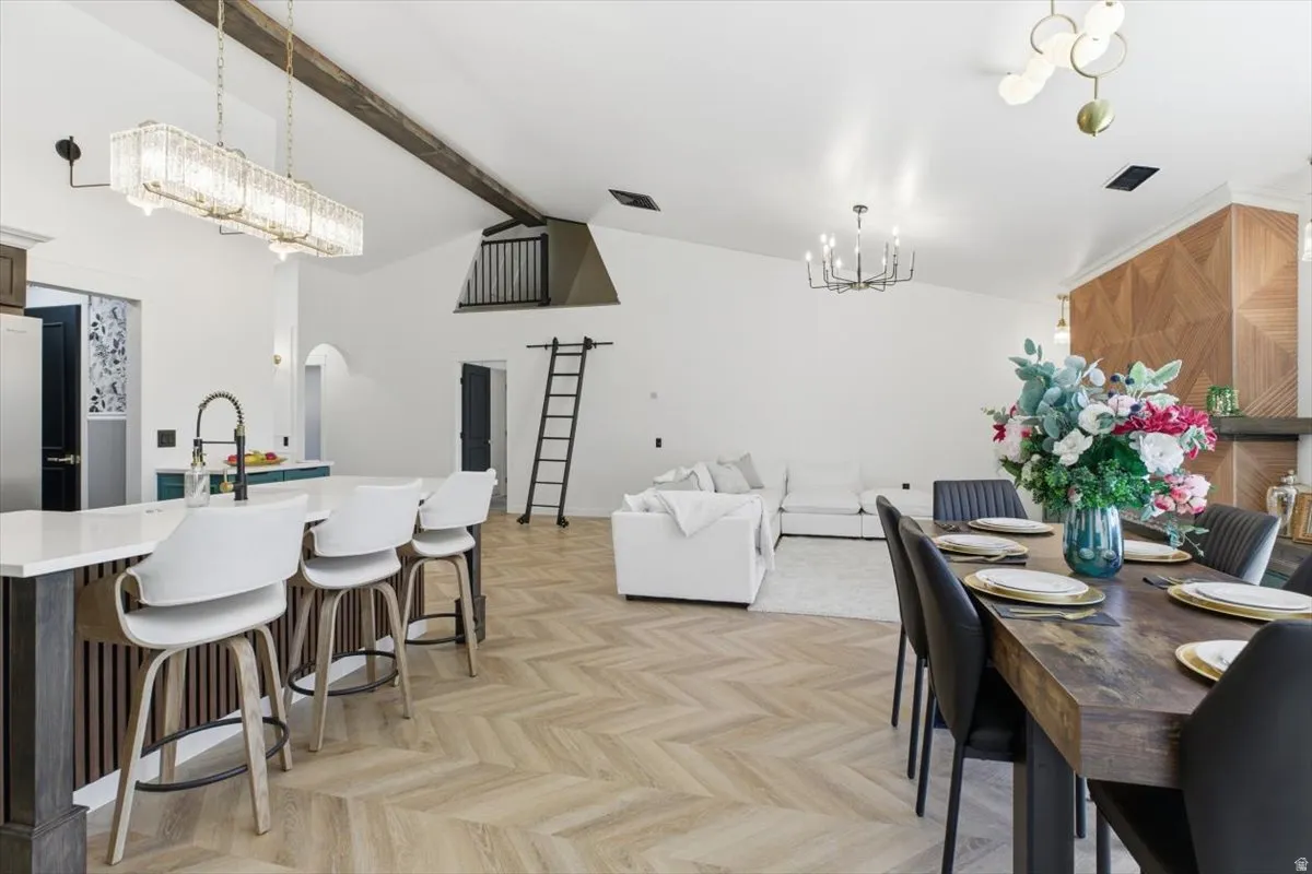 Open-concept living space featuring wood-finish herringbone flooring, vaulted ceilings with exposed beams, and a kitchen island with seating