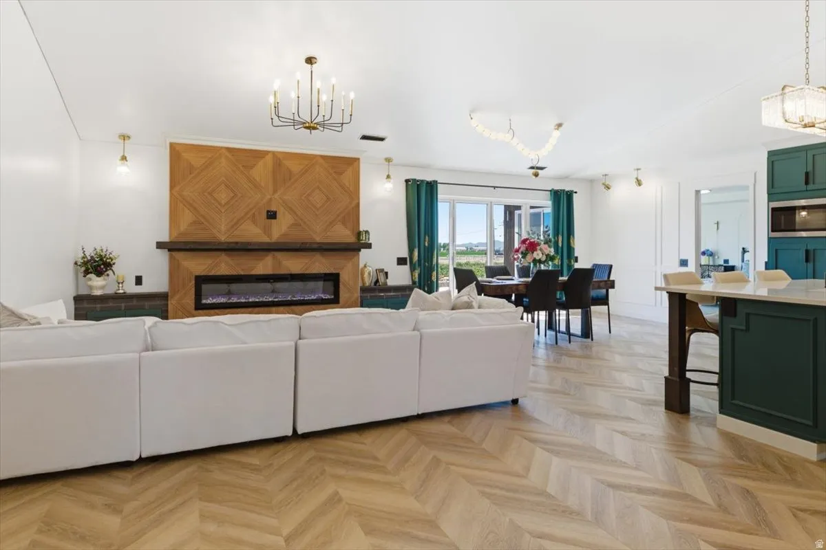 Open-concept living area featuring herringbone-pattern wood-finish flooring, a contemporary fireplace with a decorative wood accent wall, and recessed lighting
