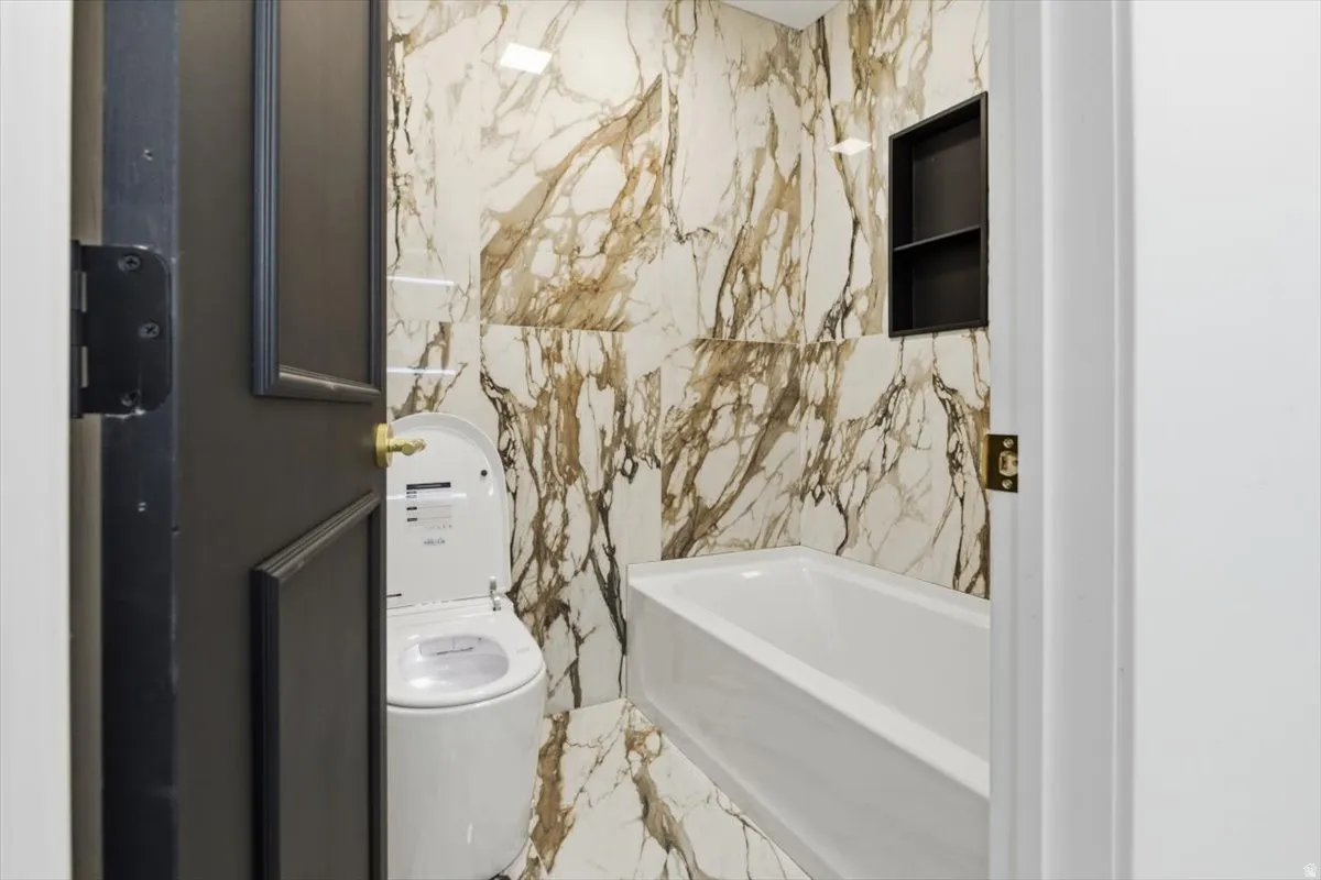 Full bathroom featuring large format veined wall and floor tiles, a white soaking tub, and a built-in shower niche