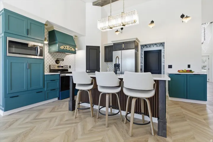 Chef's kitchen featuring teal cabinetry, stainless steel appliances, a decorative range hood, wood-finish herringbone flooring, and a central island with countertop seating