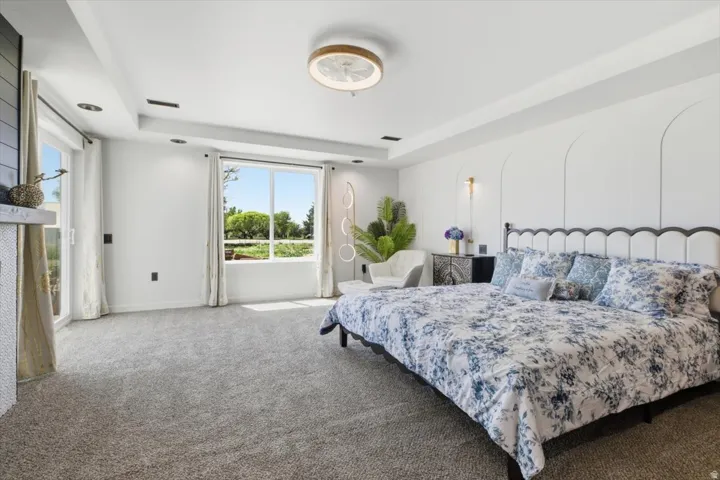 Carpeted room featuring a double tray ceiling with recessed lighting, large windows, and a built-in fireplace with a stone mantel