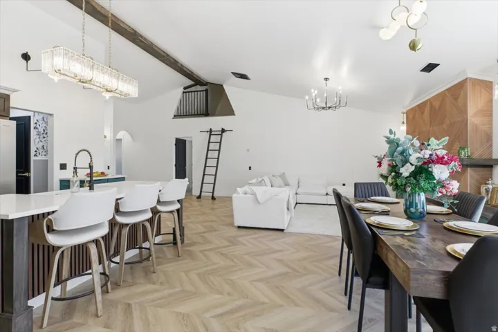 Open-concept living space featuring wood-finish herringbone flooring, vaulted ceilings with exposed beams, and a kitchen island with seating