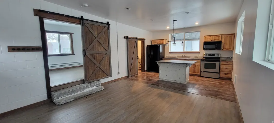 Open-concept living space featuring wood-finish flooring, a kitchen island with pendant lighting, stainless steel appliances, and two wood barn doors