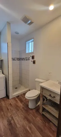 Full bathroom featuring a walk-in shower with tile surround, a single vanity with wood-finish cabinetry, and wood-finish flooring