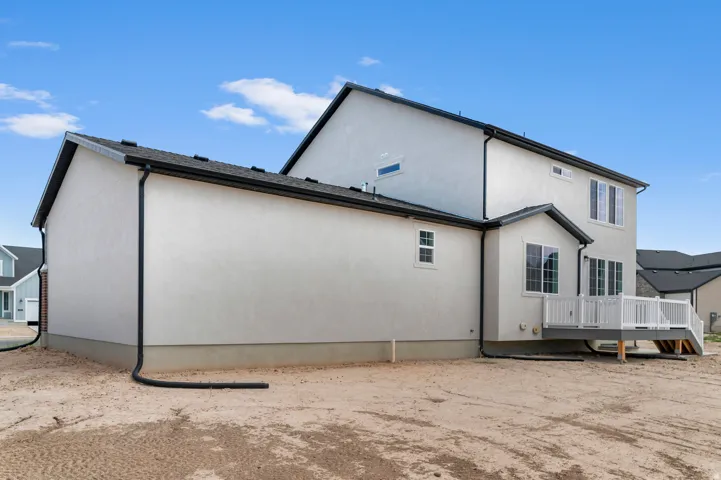 Contemporary stucco exterior with a multi-level design, dark shingle roof, black gutters, and a rear deck featuring white railings