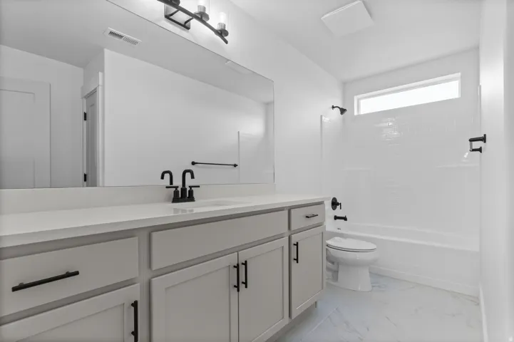 Bathroom featuring a double vanity with light-colored countertops, matte black fixtures, a large wall mirror, and a tub-shower combination with subway tile surround