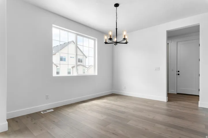 Spacious interior room featuring wood-finish flooring, white baseboards, and a modern black chandelier with clear glass shades