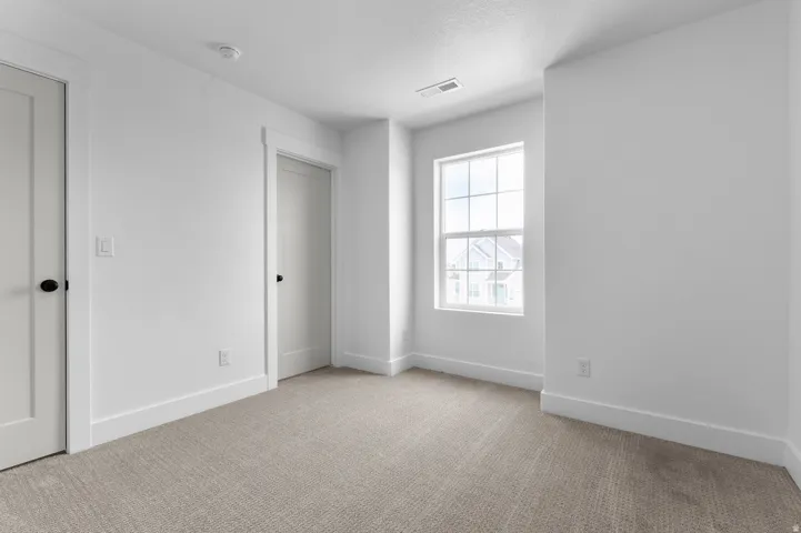 Carpeted interior space featuring light neutral walls, a double-hung window, and two doors with matte black hardware