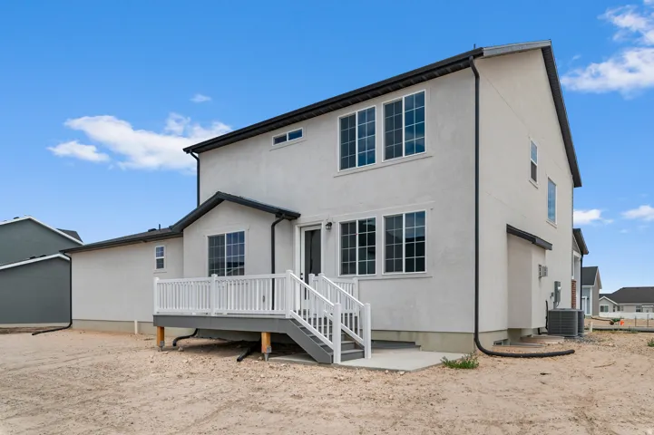 Rear facade featuring a neutral stucco exterior, multiple large windows, and a raised composite deck with white railings and stairs