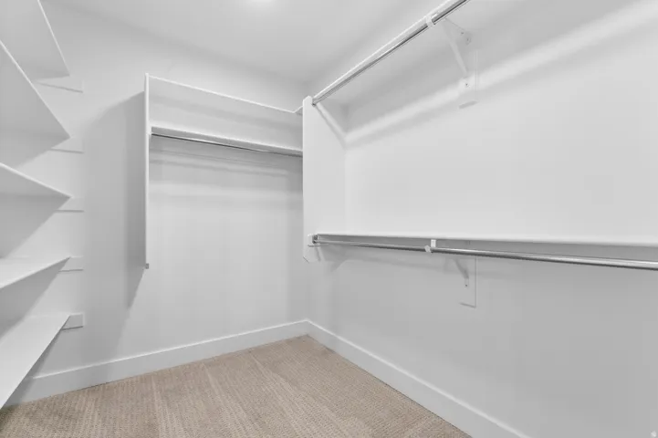Walk-in closet featuring built-in shelving, multiple hanging rods, white walls, recessed lighting, and carpet flooring