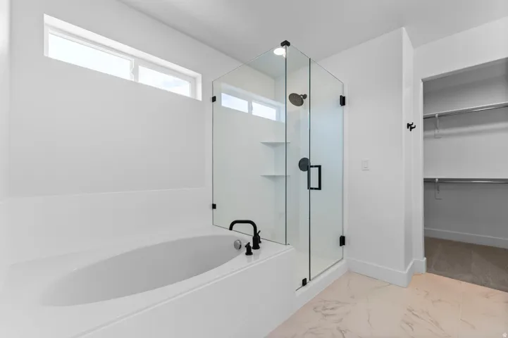 Contemporary bathroom featuring a built-in soaking tub with matte black fixtures, a glass-enclosed shower with a rain showerhead, and light-toned tile flooring