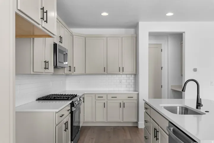 Modern kitchen featuring light gray cabinetry, stainless steel appliances, white subway tile backsplash, light-toned countertops, and wood-finish flooring