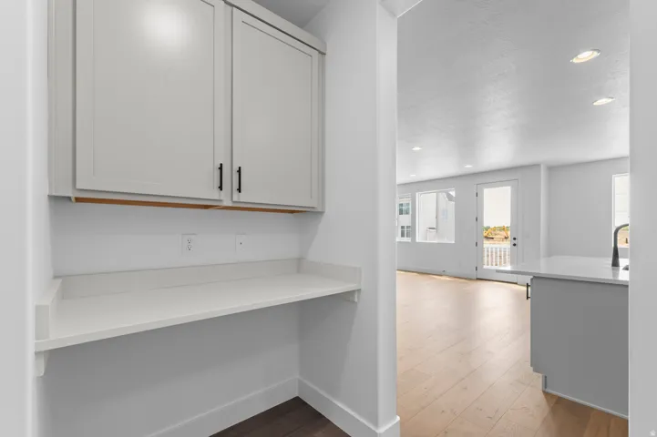 Built-in desk alcove featuring light gray cabinetry with black hardware, a white countertop, and integrated electrical outlets