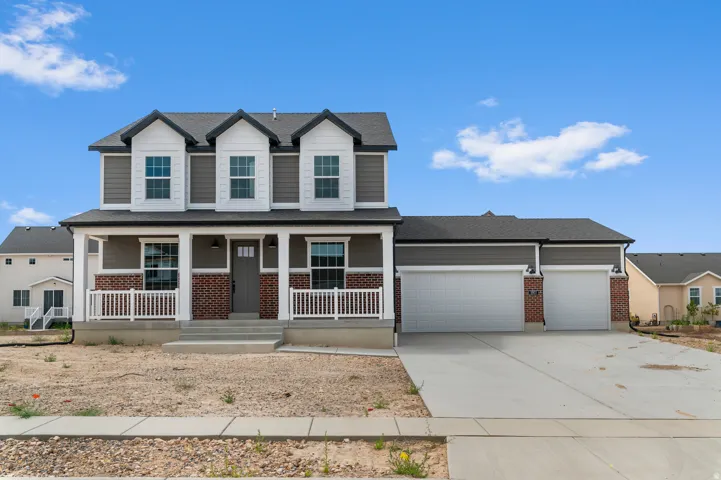 Two-story residence featuring a covered front porch with white railing, dormer windows, and a two-car garage with concrete driveway