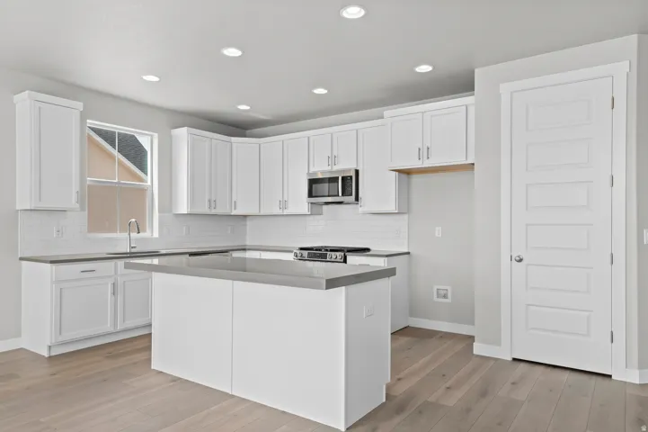 Kitchen featuring white shaker cabinetry, light wood-finish flooring, a central island with countertop, stainless steel appliances, and recessed lighting