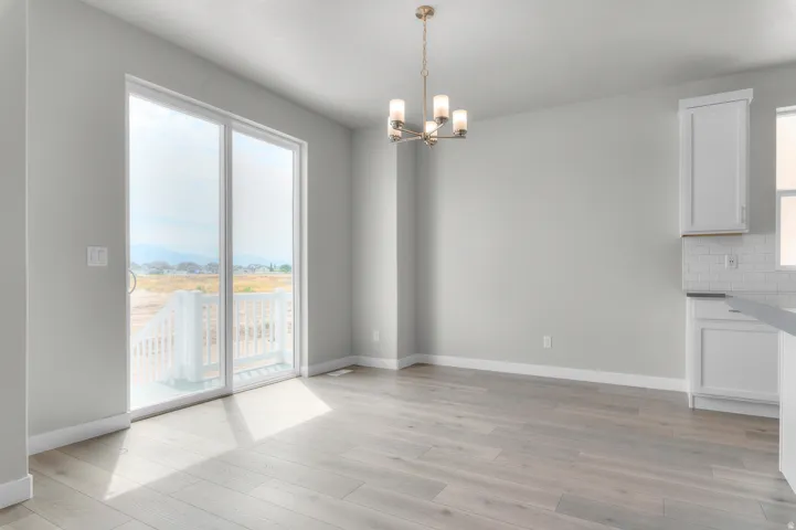 Bright interior space featuring light wood-finish flooring, a contemporary chandelier, and large sliding glass doors opening to an outdoor deck with white railings