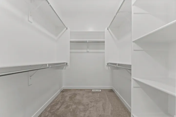 Walk-in closet featuring extensive shelving and hanging rods, white walls, and neutral carpet flooring