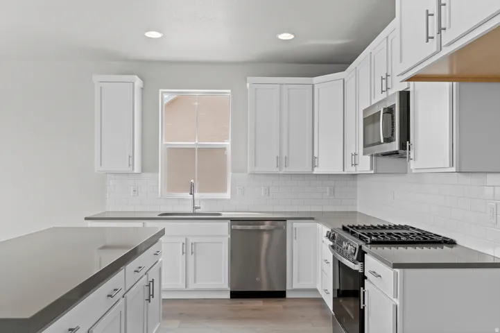 Modern kitchen featuring white shaker cabinetry, stainless steel appliances, a subway tile backsplash, and light wood-finish flooring