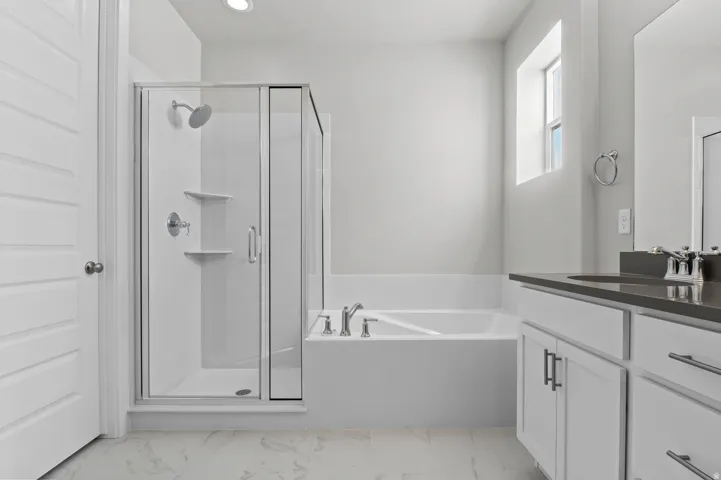 Bathroom featuring a glass-enclosed shower, a built-in soaking tub, a vanity with dual sinks, and white cabinetry with dark hardware