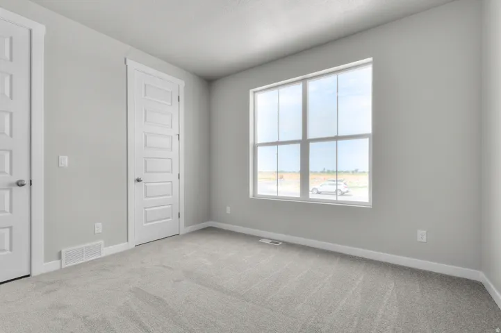 Spacious room featuring light gray carpeting, neutral wall color, and a large window providing abundant natural light