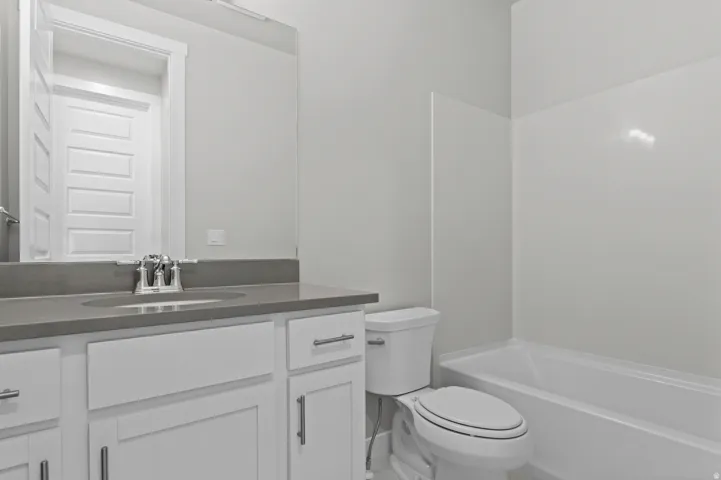Contemporary bathroom featuring a white vanity with shaker-style cabinetry, a gray solid surface countertop, and a chrome faucet