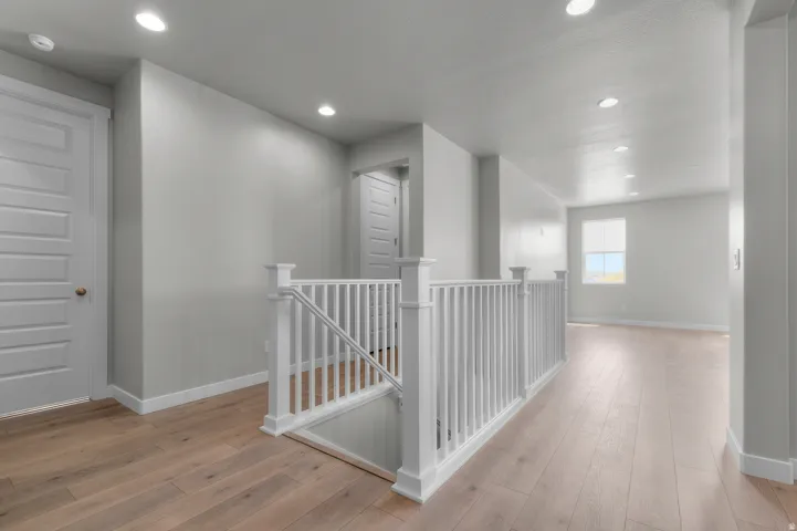 Upper-level hallway featuring a white baluster railing and wood-finish flooring