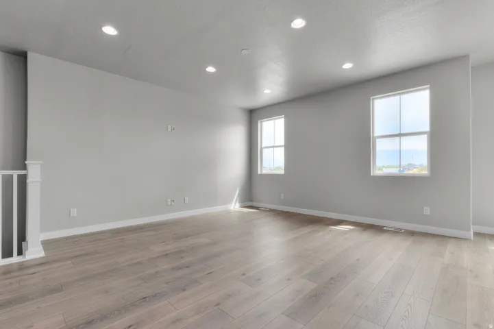Spacious room featuring light wood-finish flooring, recessed ceiling lighting, and multiple windows with white trim