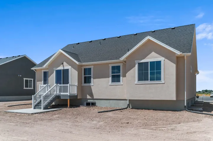 Rear exterior featuring a neutral stucco finish, white trim, and a dark shingle roof