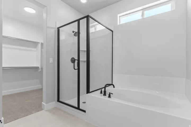 Bathroom featuring a glass-enclosed shower with matte black fixtures, an adjacent built-in soaking tub with matte black faucet, and a high transom window