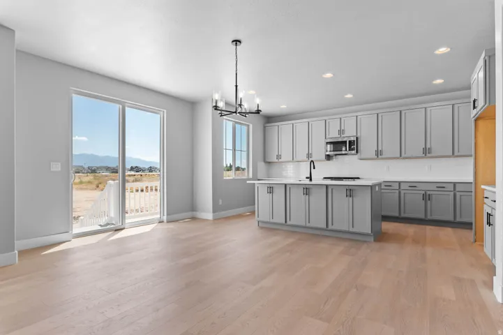 Open-concept kitchen and dining area featuring light wood-finish flooring, grey cabinetry, white countertops, and stainless steel appliances