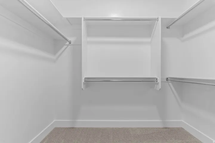 Walk-in closet featuring white built-in shelving, multiple chrome hanging rods, and light-toned carpeting