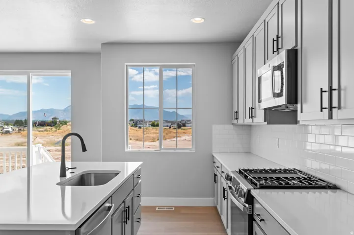 Modern kitchen featuring a stainless steel sink, black gooseneck faucet, light grey cabinetry, white countertops, and a subway tile backsplash