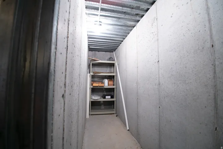 Unfinished basement utility space featuring concrete walls, a corrugated metal ceiling, and a built-in shelving unit