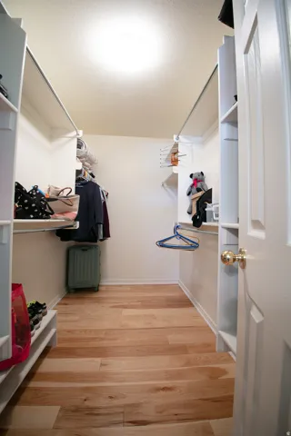 Walk-in closet featuring light wood-finish flooring, white built-in shelving, hanging rods, and a ceiling-mounted light fixture