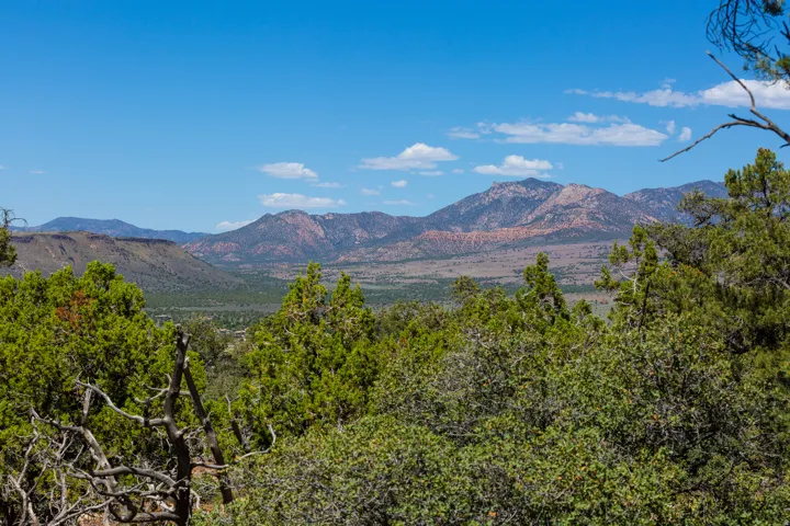 Expansive mountainous landscape with a verdant valley, natural tree lines, and a vast blue sky with scattered clouds