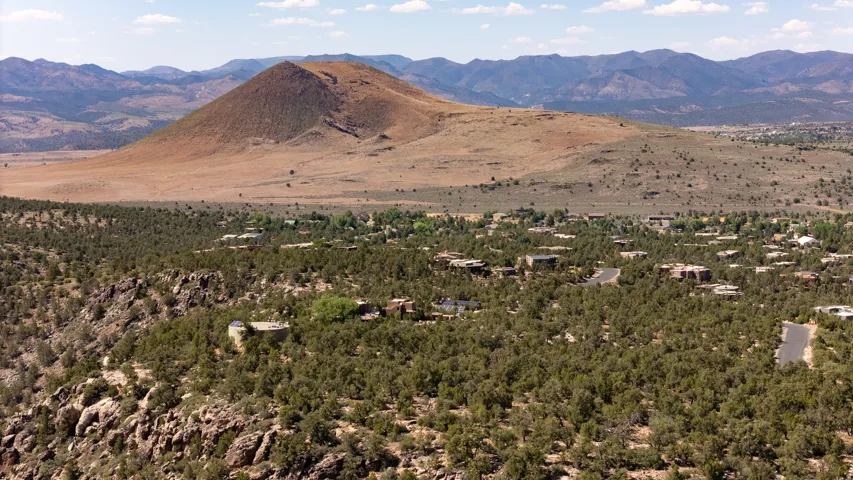 Expansive desert landscape with a prominent conical hill, surrounded by a verdant forest