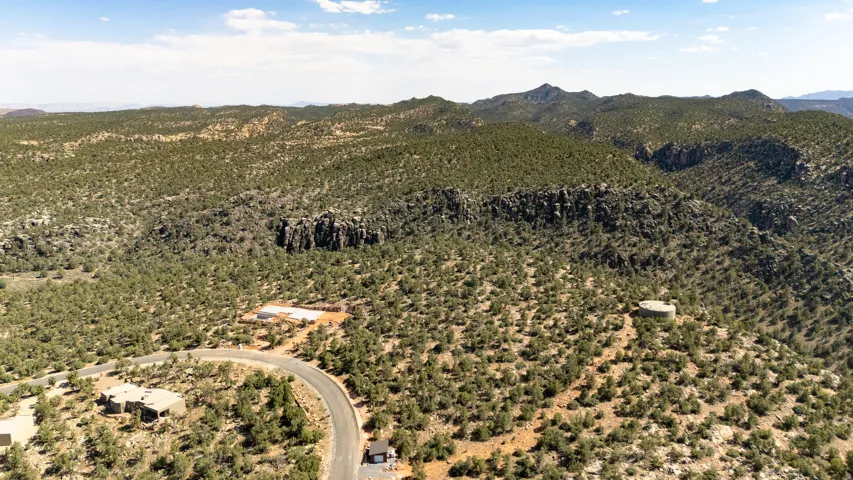 Expansive desert landscape featuring rolling hills, scattered green vegetation, and distant mountain ranges under a clear sky