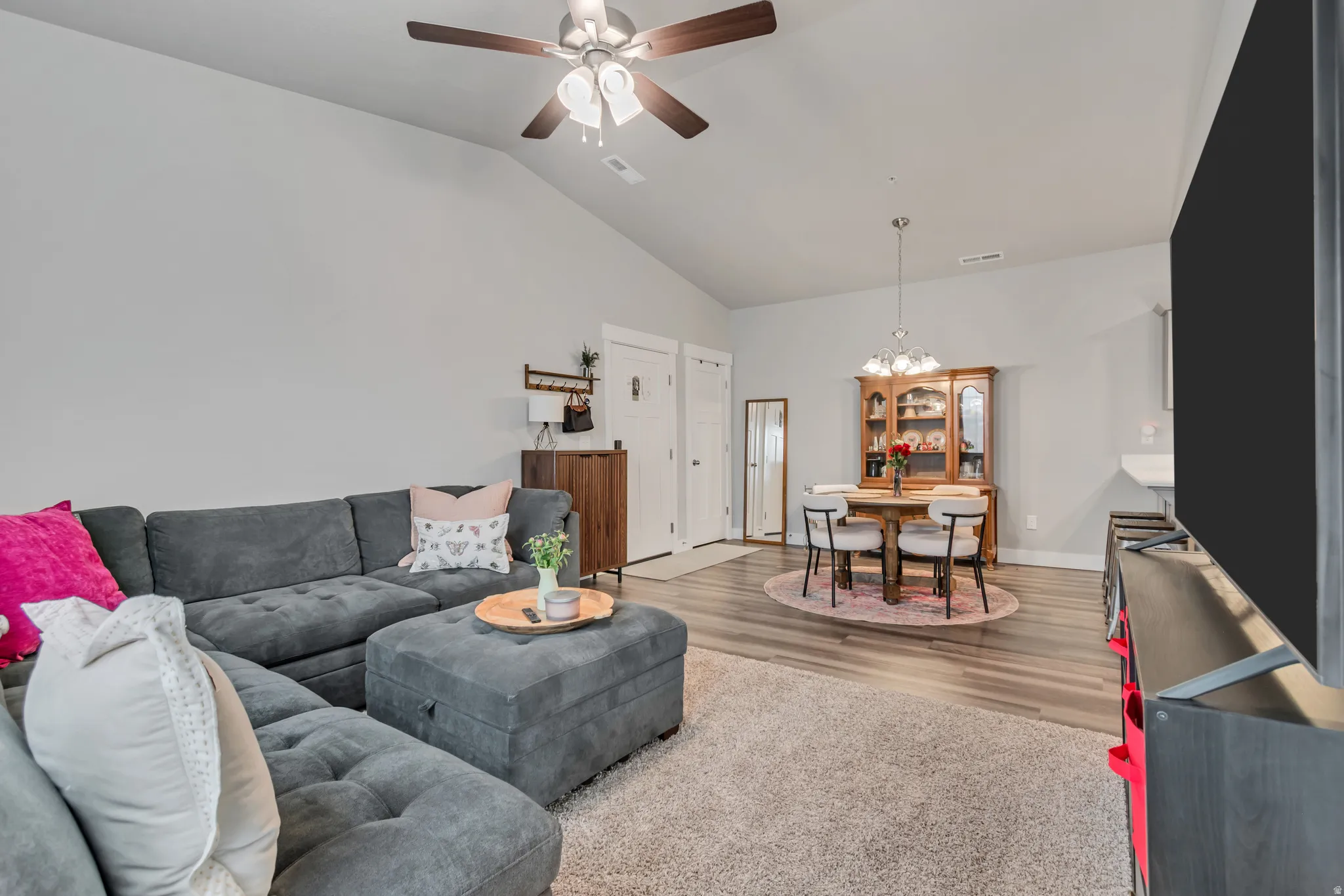 Vaulted ceiling with a ceiling fan, wood-finish flooring, and a built-in fireplace mantel