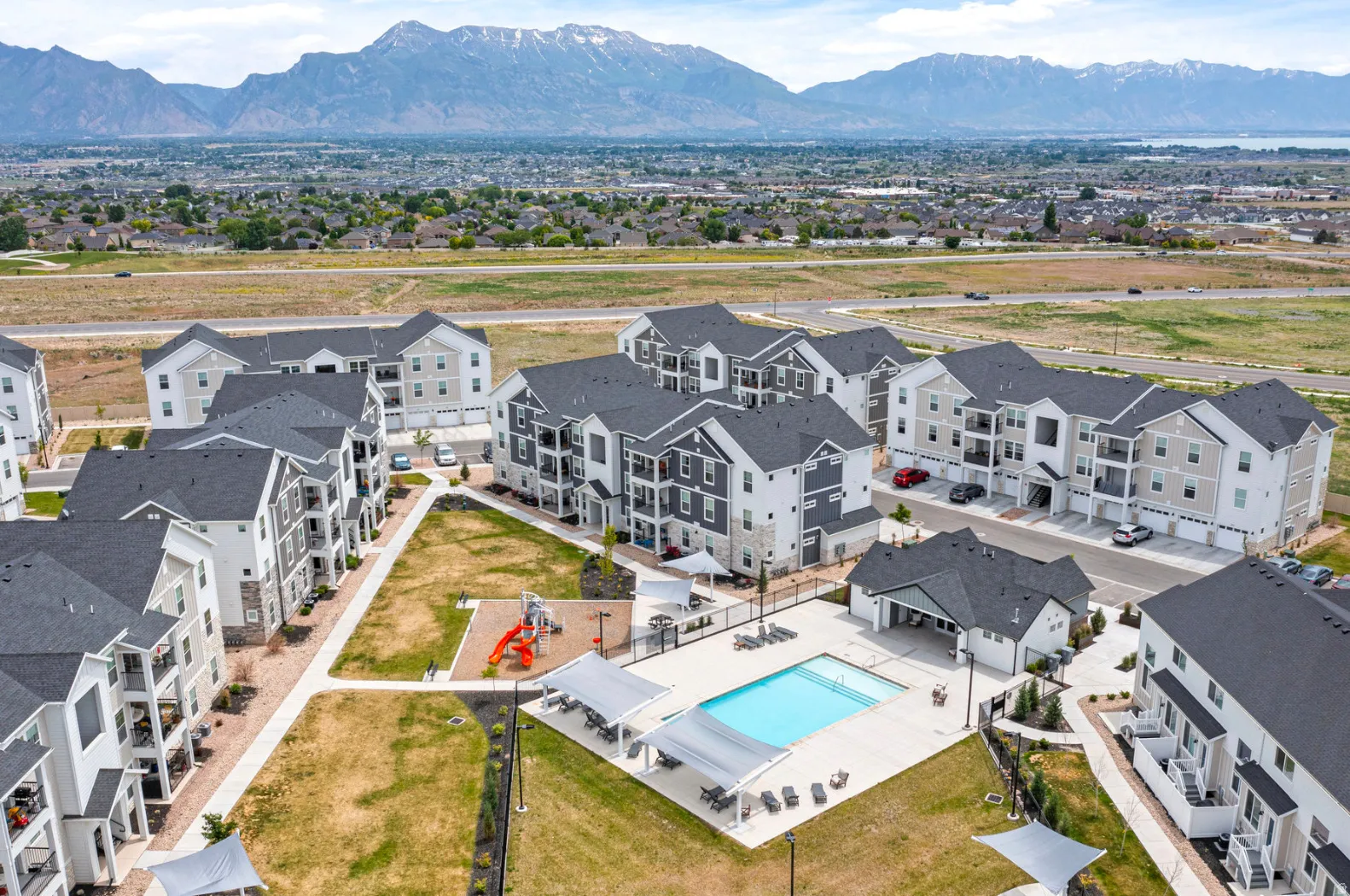 Community grounds featuring multiple residential buildings, an outdoor swimming pool, a playground, and expansive green spaces