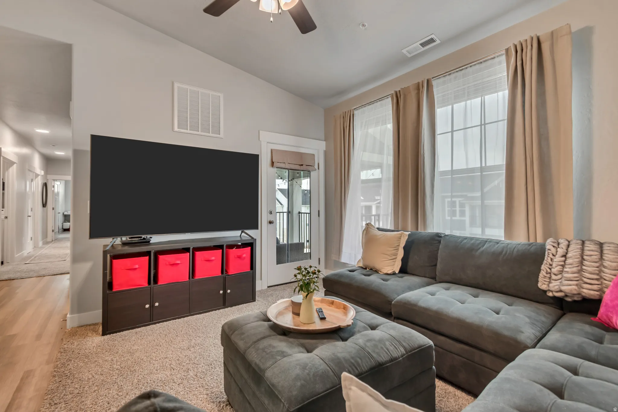 Living area featuring a textured carpet, a ceiling fan, and a hallway with wood-finish flooring