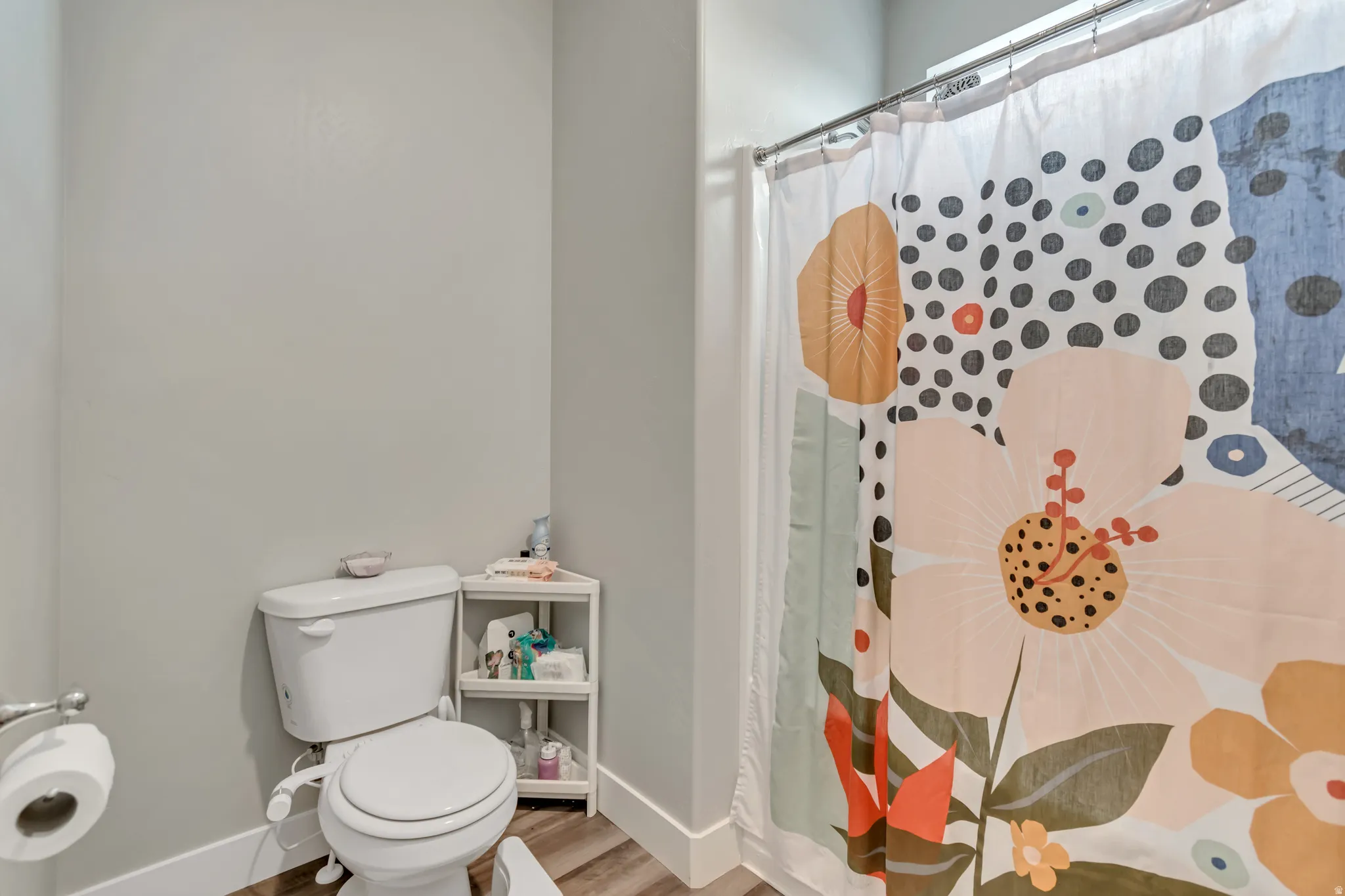 Shower with a stainless steel curtain rod, a white toilet, and wood-finish flooring