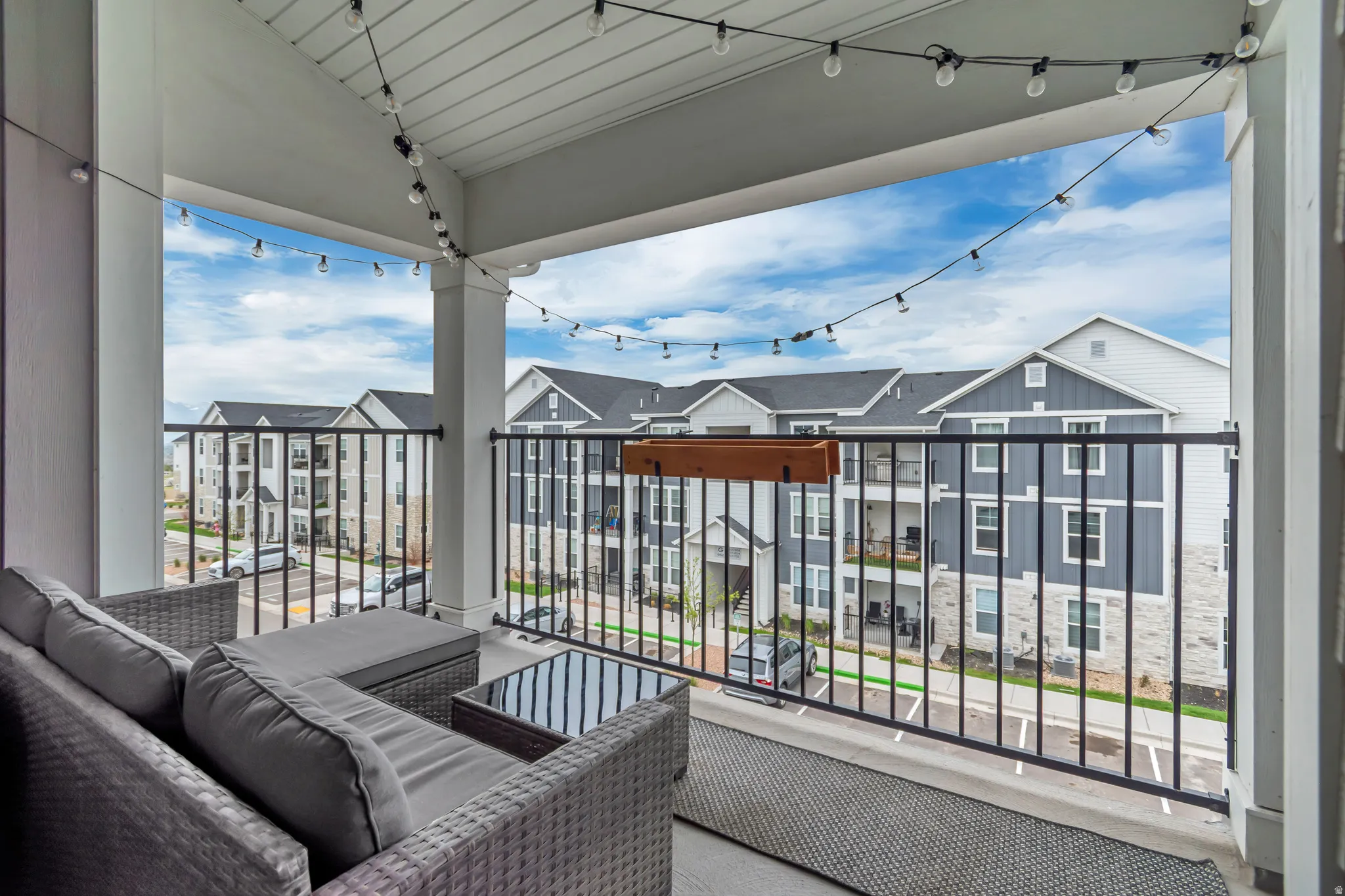 Expansive covered balcony featuring a black metal railing, string lighting, and a wood planter box