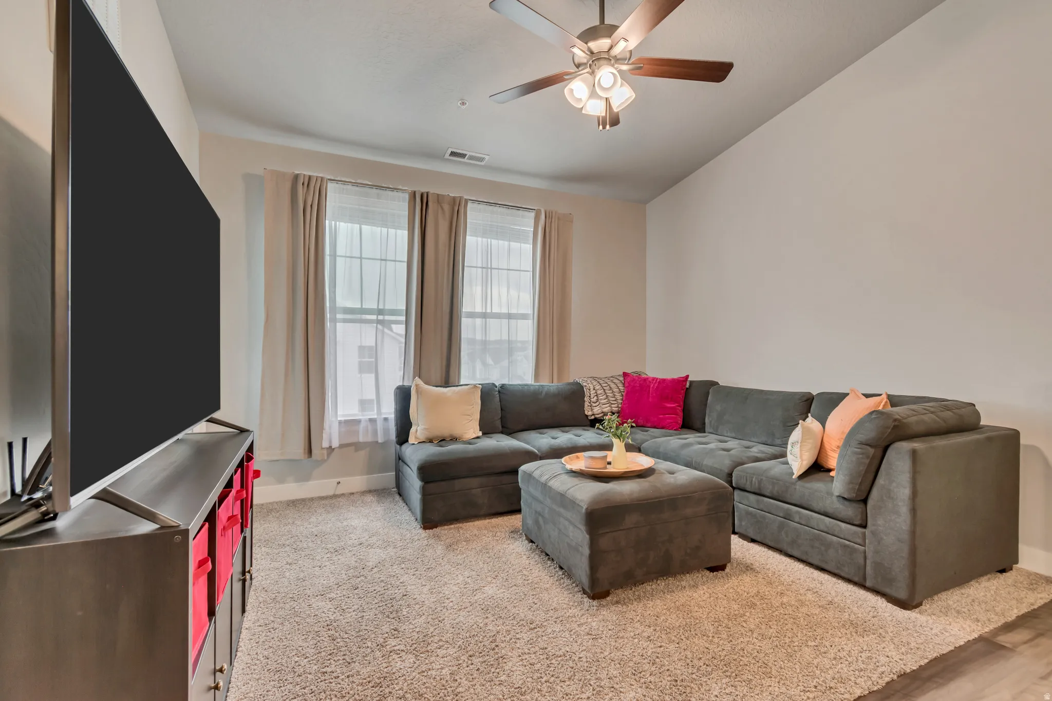 Inviting living area featuring vaulted ceilings, a ceiling fan with light fixture, triple windows with natural light, and soft carpeting