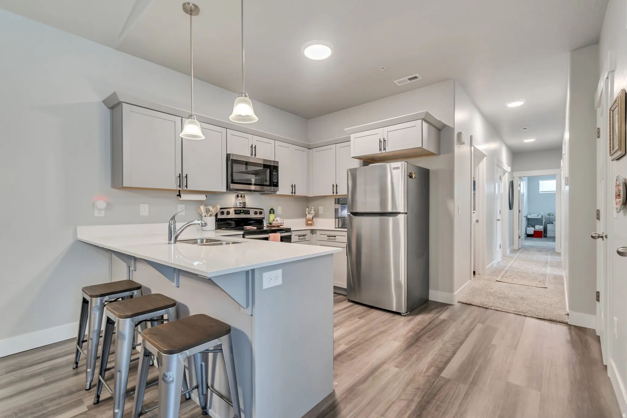 Modern kitchen featuring light gray cabinetry, stainless steel appliances, a white countertop, and wood-finish flooring